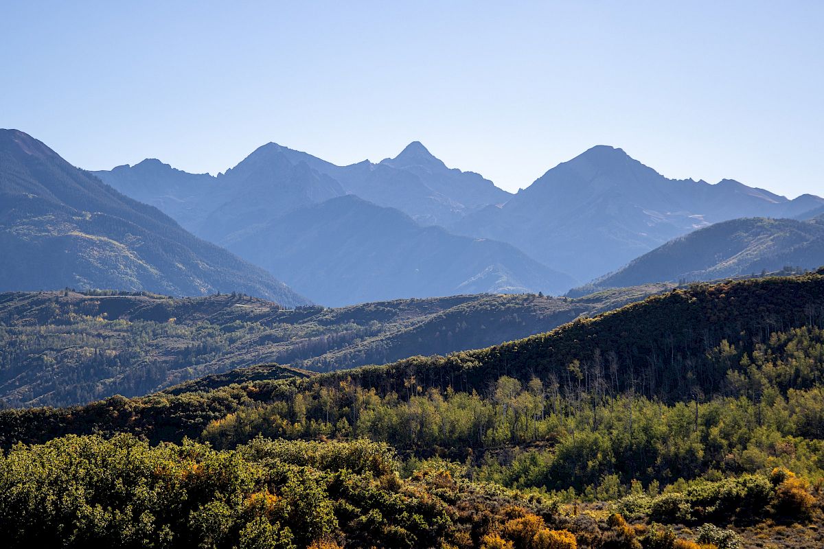 Breathtaking mountain range with layered ridgelines and forested hills under a clear blue sky.