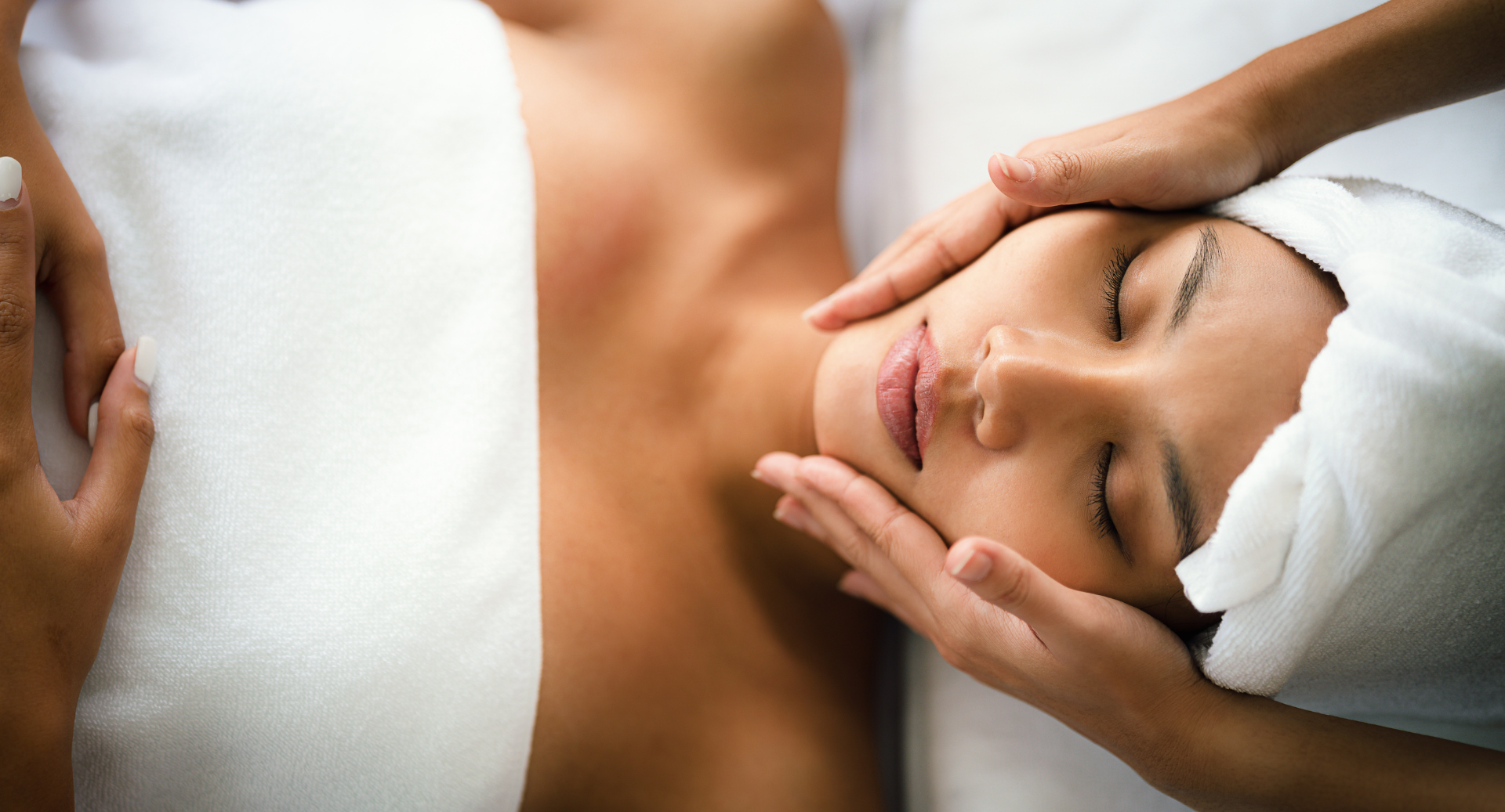 A therapist gives a relaxing face massage, hands smoothing the client&rsquo;s forehead under a soft towel.