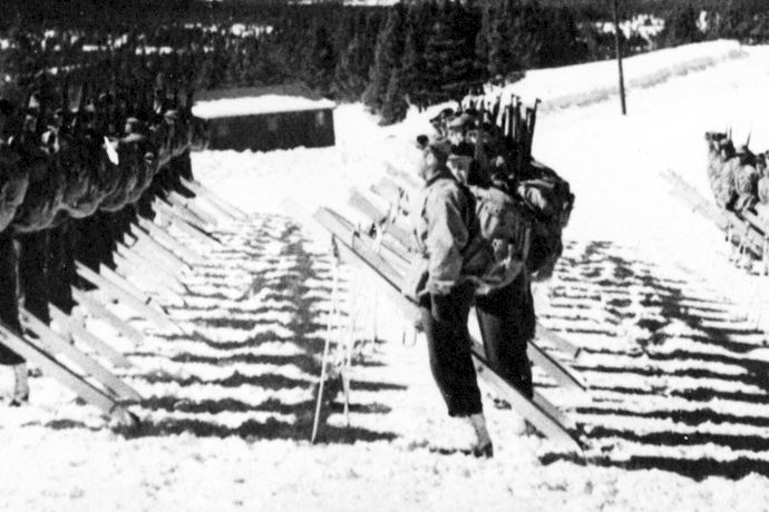 A line of soldiers in snowy terrain marches with rifles along a mountain track, preparing for combat.