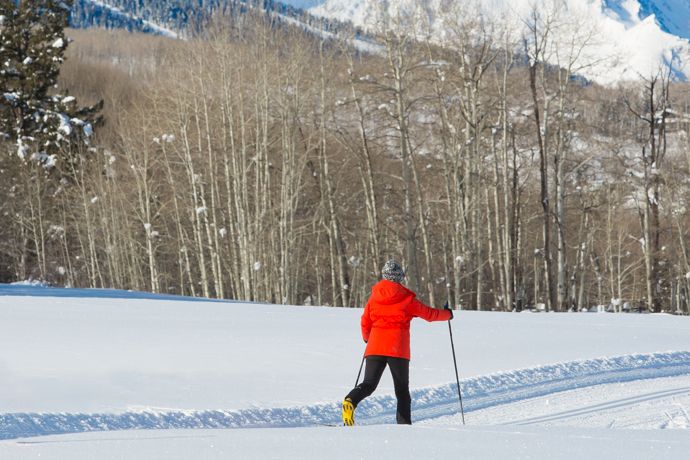 Two skiers in bright jackets glide across snowy fields in a mountain valley under blue winter skies.