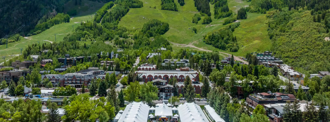 Aerial view of a Swiss-style mountain village with large white festival tents and crowds in a green valley.
