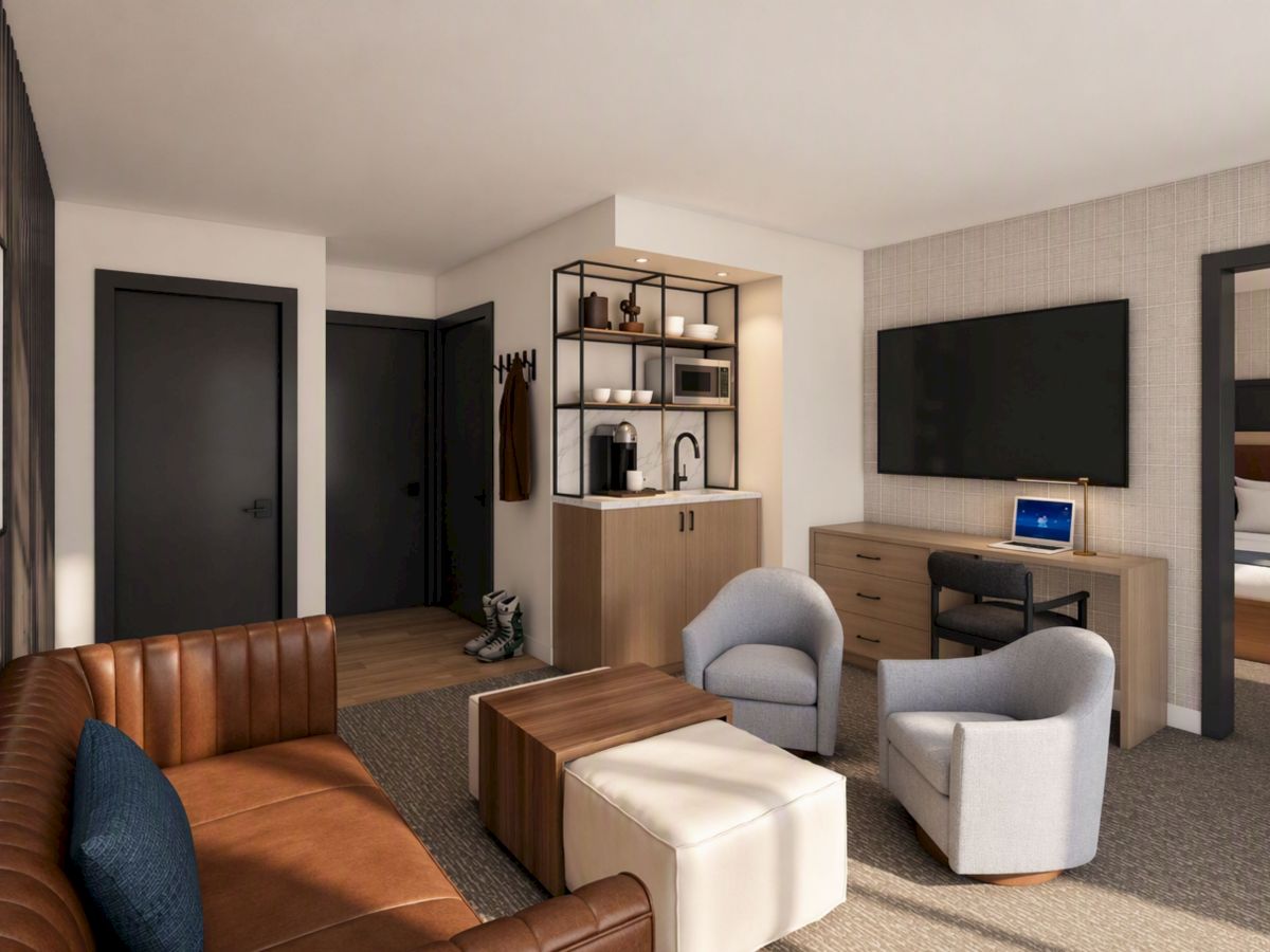 Modern hotel lounge with a leather sofa, coffee table, wall TV, desk with laptop, and built-in bar shelves with coffeemaker.