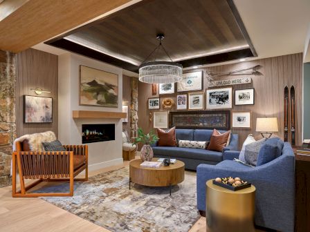 Cozy ski-themed living room with a fireplace, chandelier, blue sofa, framed photos, and stacked skis.
