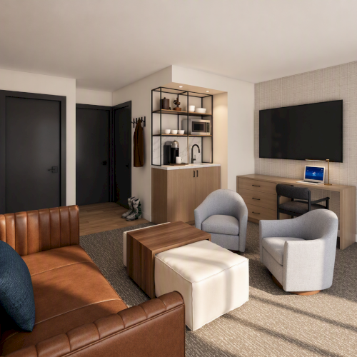 A modern hotel suite lounge with brown leather sofa, coffee table, desk setup, and built-in wet bar shelving, plus a bedroom visible through an open door.