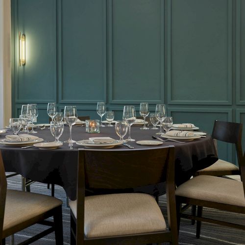 An elegantly set dining table with wine glasses, plates, cutlery, and a small candle in a softly lit room.
