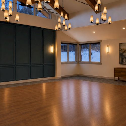 An elegant room with dark paneled wall, warm pendant lights, windows, artworks, and wooden console and floor.