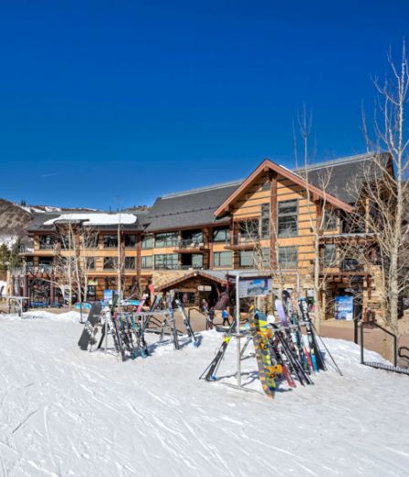 A snowy ski resort lodge with rental skis lined up outside on a bright winter day.