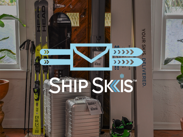 A ski gear setup with &ldquo;SHIP SKIS&rdquo; text&mdash;skis, boots, and silver suitcases packed by a door beside ski boxes and branding.