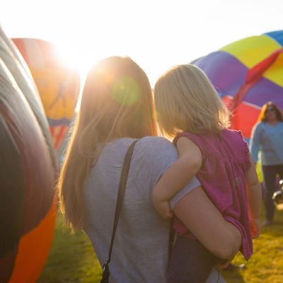 A group of kids at an outdoor festival at sunset, with colorful inflatable tents and a rainbow-themed backdrop.