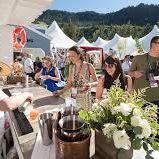At an outdoor ceremony, people in hats and sunglasses mingle near a table with flowers and a judge&rsquo;s podium.