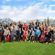 Group photo of many people outdoors on a sunny lawn, smiling and standing in rows with trees and sky behind them.