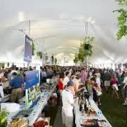 A busy outdoor market event with people browsing booths and long tables under white tents.
