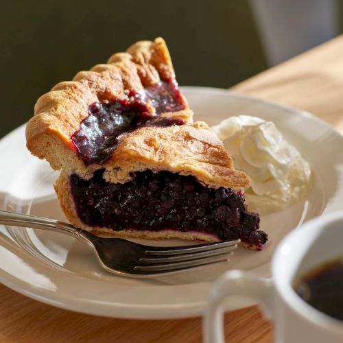 A slice of cheesecake or pie with a blueberry filling, served on a plate with a bit of whipped cream.