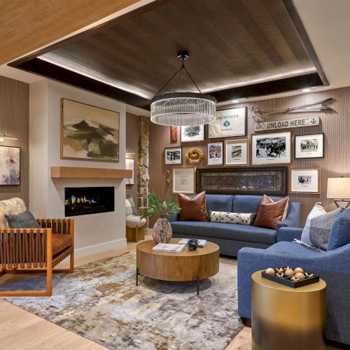 Cozy modern living room with a blue sofa, fireplace, stone wall, framed photos, and a hanging chandelier light.