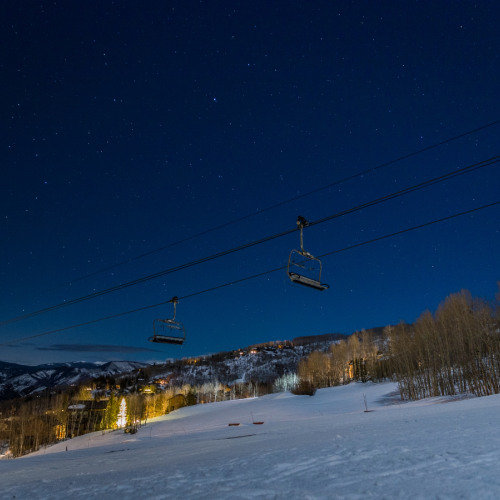 A ski resort at night with cable-suspended gondolas over snowy slopes under a starry sky.