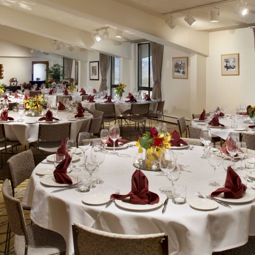 Elegant banquet room set for a formal dinner: white tablecloths, red napkins, floral centerpieces, and lots of wine glasses.