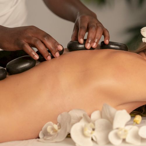 A therapist uses smooth hot stones to massage a client's bare back during a relaxing spa session.