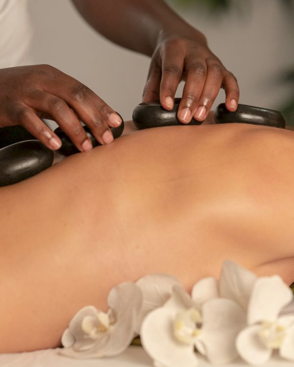 A therapist uses smooth hot stones to massage a client's bare back during a relaxing spa session.