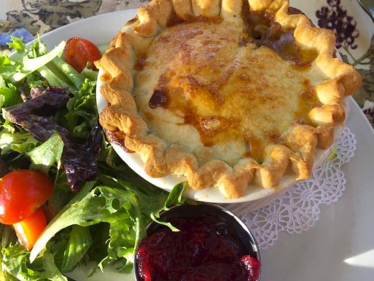 A baked golden pot pie with a side salad (greens and tomatoes) and a small bowl of dark beet sauce.